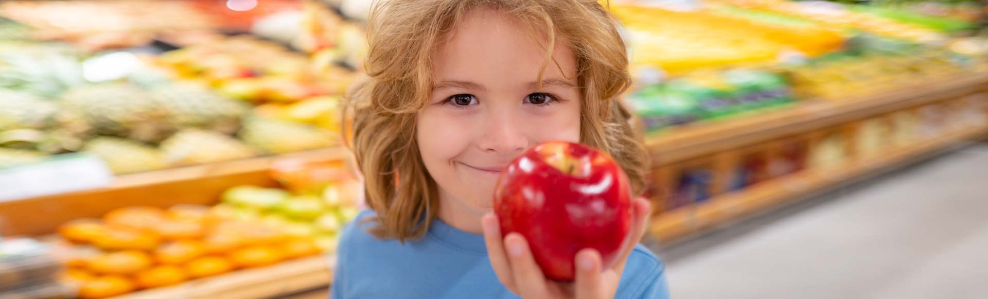 Girl holding an apple in a grocery store.